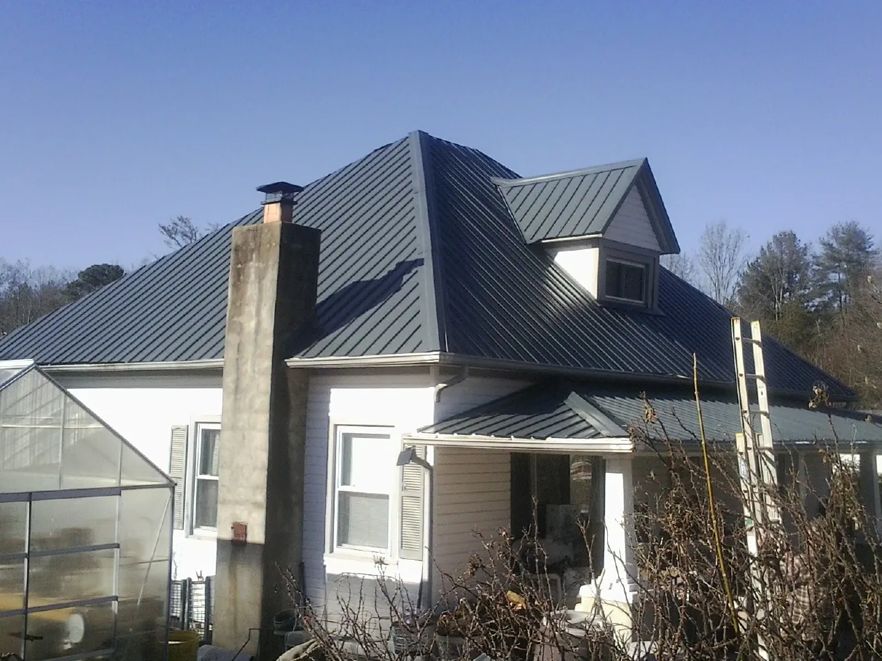 Dark blue standing seam metal roof on a white farmhouse with dormer — Slate & Tile Roof Repair by Roofing Brothers in Osawatomie