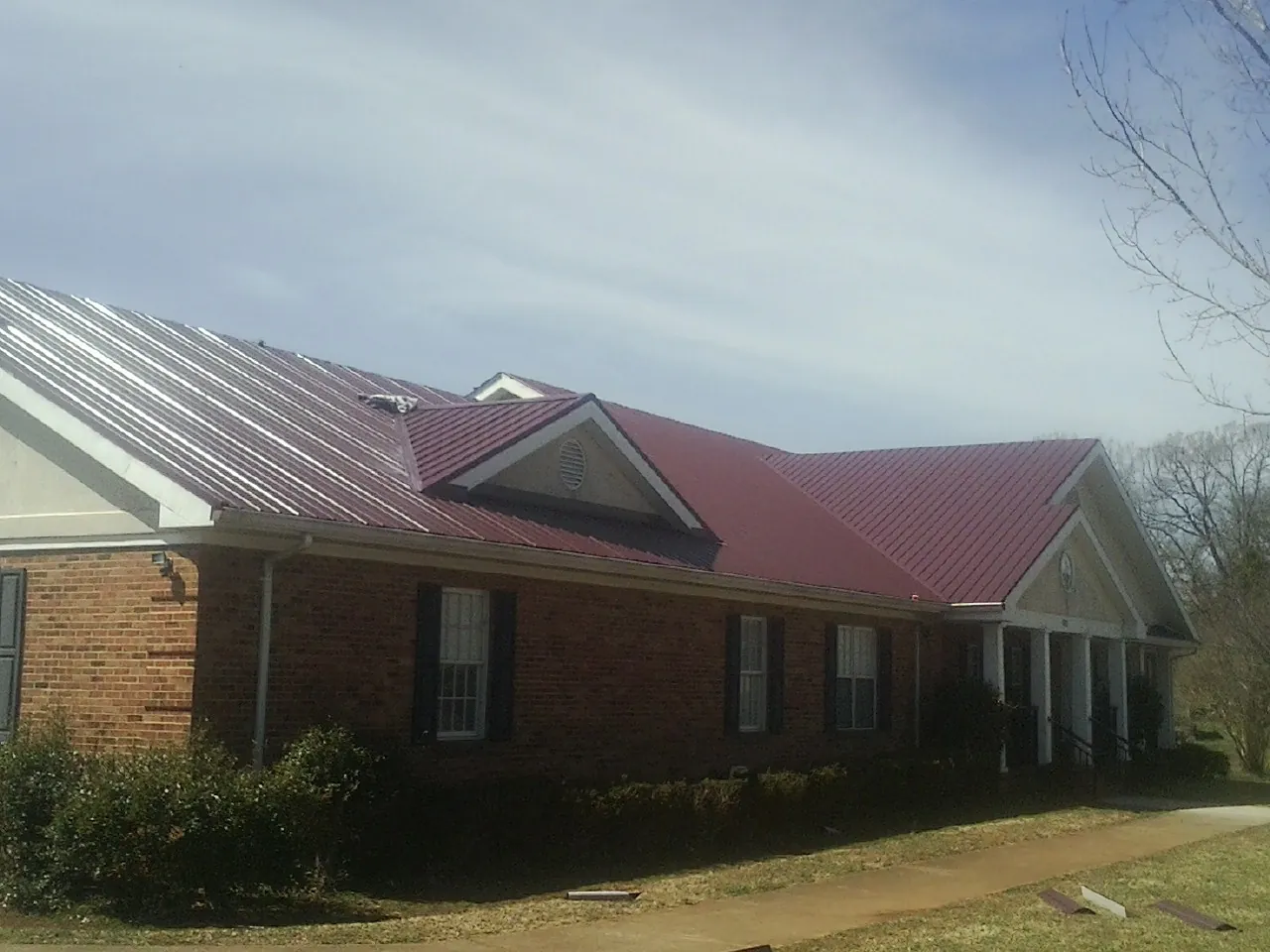 Red metal roof with gabled entries on a long brick building, from a Hail Damage Roof Repair job in Osawatomie