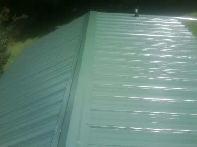 New green metal panels meeting at the ridge of a roof — Flat Roof Repair work by our crew in Osawatomie