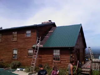Green metal roof going on a two story log home with ladders set in Osawatomie