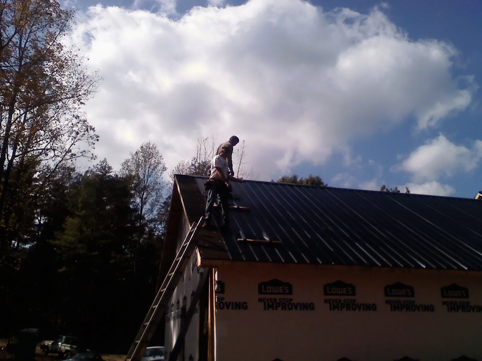 Roofer fastening dark metal panels high against a cloudy sky, from a Roof Inspection job in Osawatomie