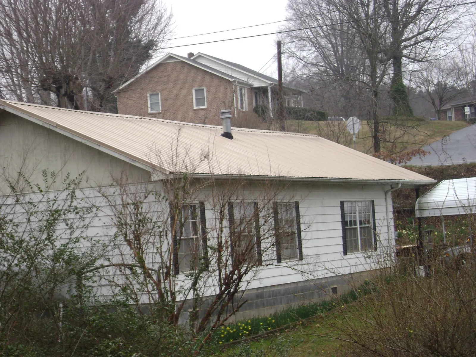 Tan metal roof on a white sided house set into a hillside — Commercial Roofing by Roofing Brothers in Osawatomie