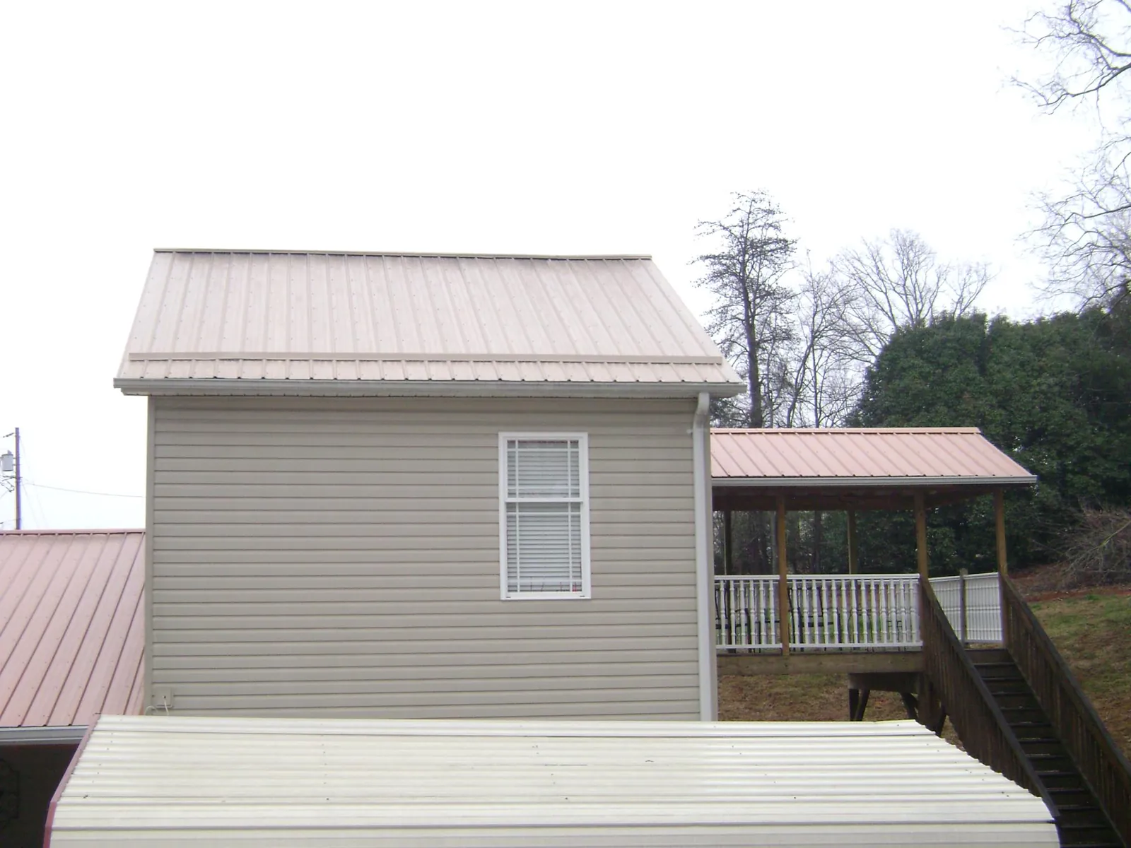 Tan metal roofs on a two story addition and attached porch, from a Roof Replacement job in Osawatomie